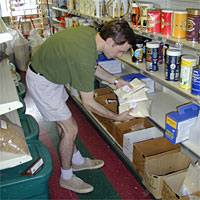 Man in green shirt and shorts selecting items from a shelf in a store.