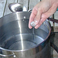 Hand holding a thermometer over a pot of water on a wooden surface.