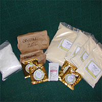 Packets of different powders, some in clear plastic and others in gold foil, arranged on a dark green surface.