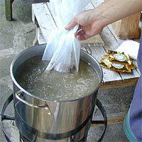 Hand lowering a bag into a large pot of boiling water on a stove, with two packages on a wooden table nearby.