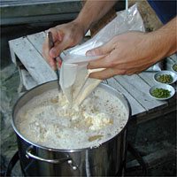 Person pouring powder into a large pot on a stove, with small bowls of ingredients nearby.
