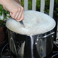 A hand stirs a large pot filled with foamy liquid that's bubbling over the top.