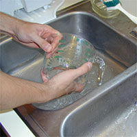 Person washing a glass measuring cup in a kitchen sink filled with water.