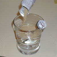 Yeast being poured into a glass of water with a thermometer, showing preparation for mixing or fermentation.