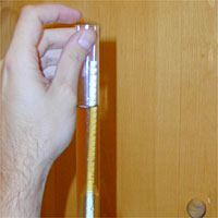 Hand holding a transparent tube containing a golden colored liquid, against a wooden background.