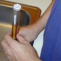 Person holding a cylinder with a liquid, standing by a sink.
