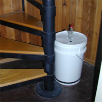 Spiral staircase with wooden steps next to a white bucket beside a wooden wall.