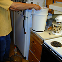 Person holding a large white bucket on a kitchen counter near appliances and cabinets.