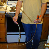 Person holding a clear plastic racking cane and a spring clamp with orange handles in a kitchen setting.