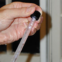 A hand holding a clear plastic racking cane with a black plastic tip, against a blurry background.