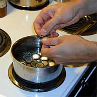 Hands placing bottle caps into a pot of water on a stove.
